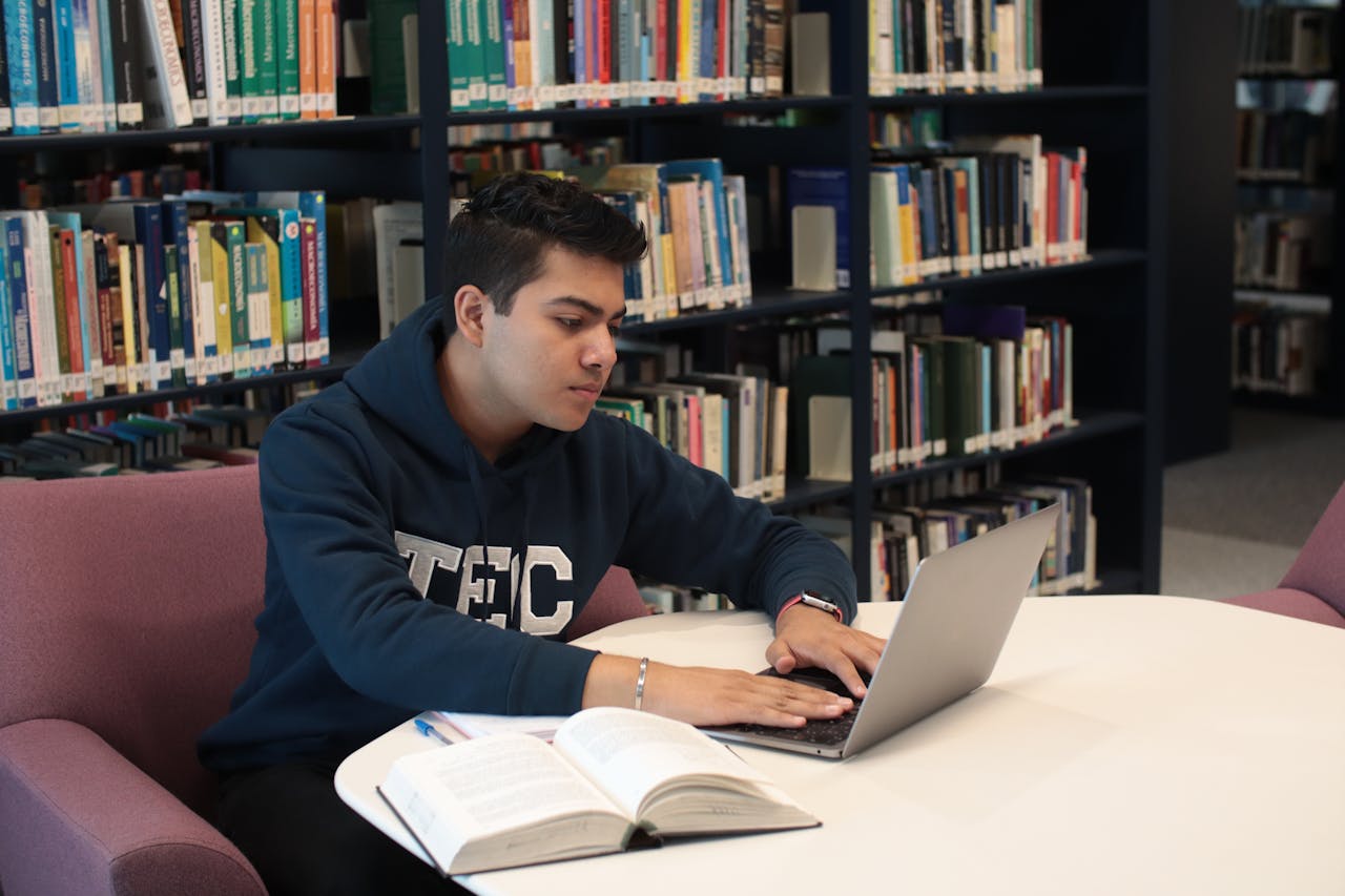 portfolio-08 Student in library using laptop and textbooks for study and research.