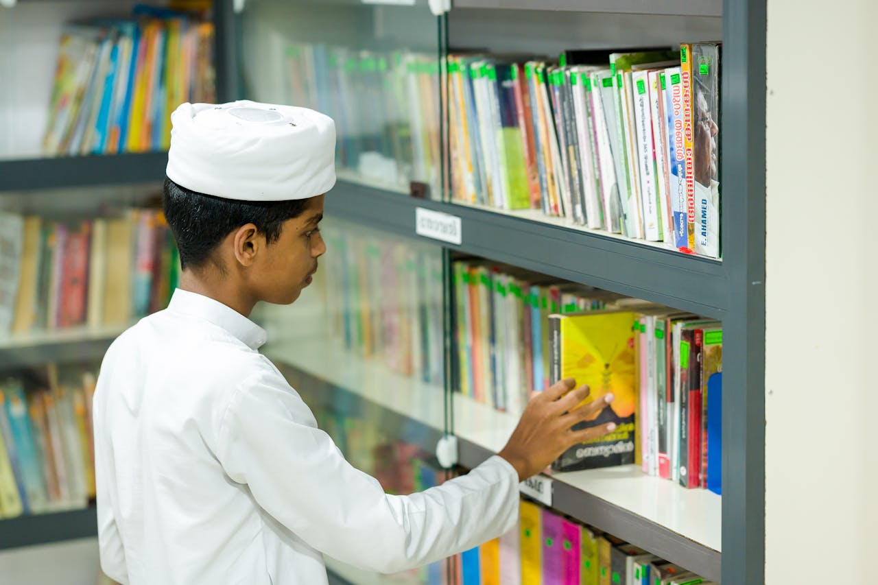 portfolio-02 A child in traditional attire picks a book from a well-organized library shelf.