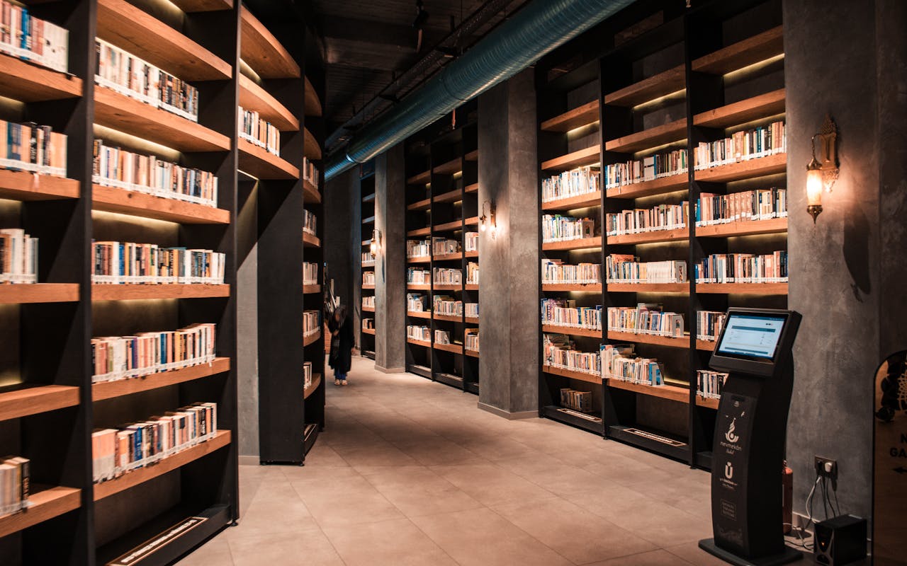 portfolio-05 A spacious library featuring tall wooden bookshelves filled with books and ambient lighting.