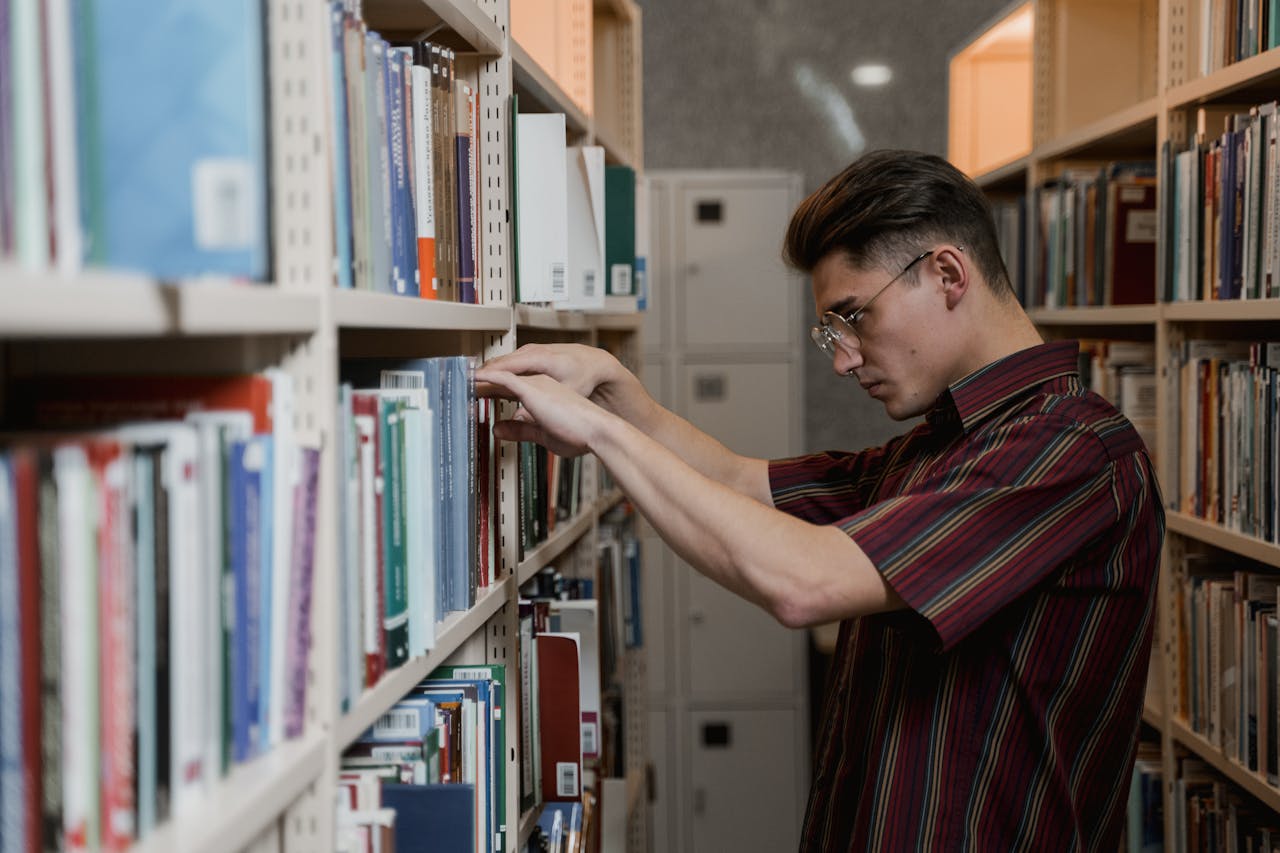 portfolio-03 A young man in glasses searches library shelves for academic resources.